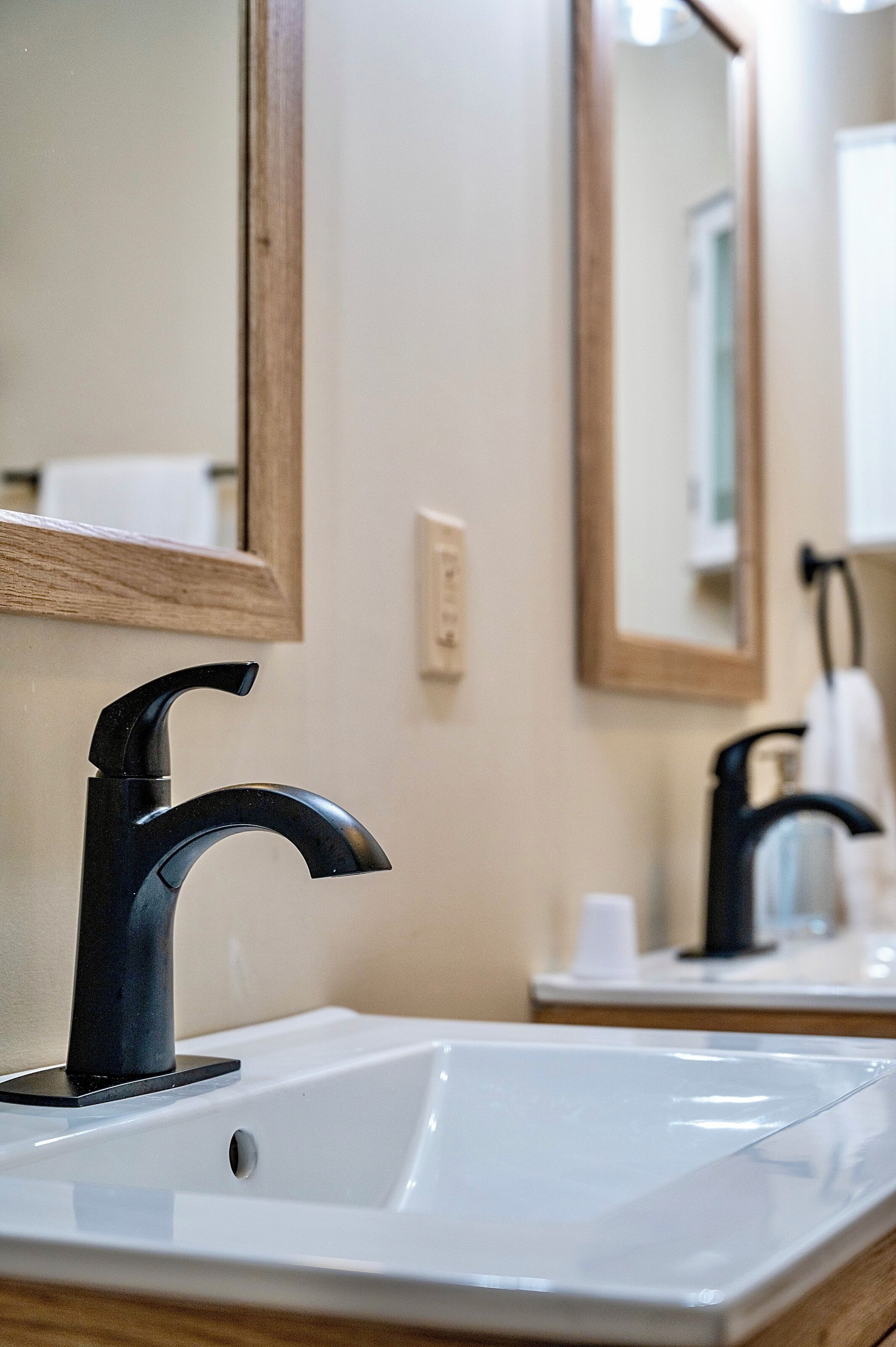 Une salle de bain avec un lavabo blanc, un robinet noir et un miroir encadré en bois.