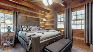 Un dormitorio de cabaña de madera con una cama, mesitas de noche y un banco.