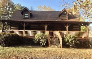 Step into this charming cabin, featuring a spacious porch with a wooden railing and dormer windows above.