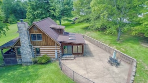 A log cabin with a stone chimney, a covered porch, and a patio area with outdoor seating.