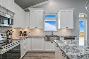 A modern kitchen with white cabinetry, a stainless steel sink, and a large window providing a view of the outdoors.