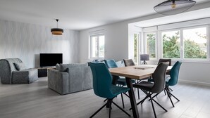 Een moderne woonkamer met een bank, een televisie en een eethoek met stoelen en een tafel.