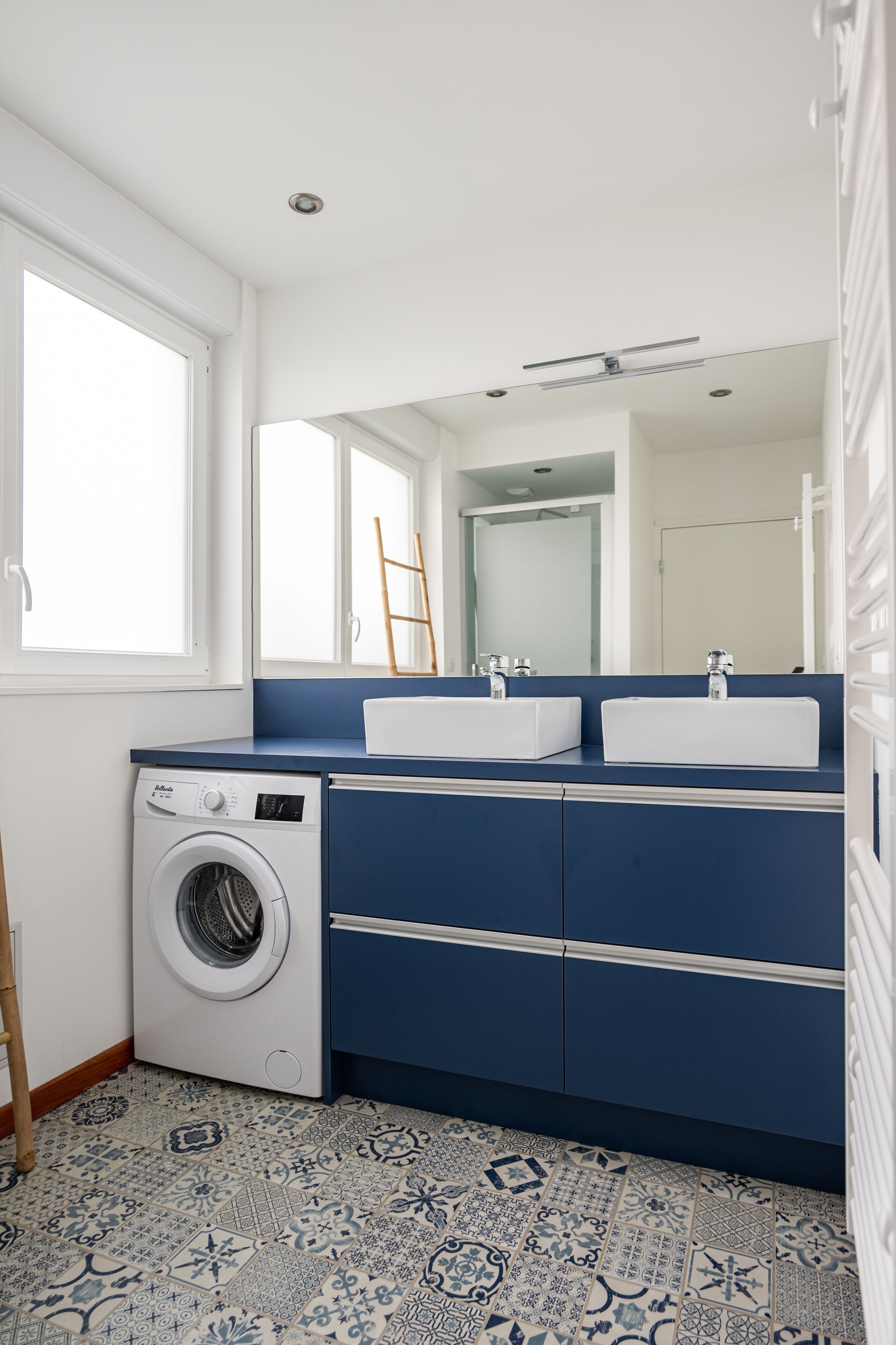 A compact laundry room with a washing machine, two sinks, and a large mirror.