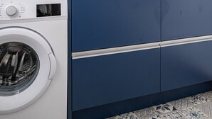 Een moderne badkamer met een witte wasmachine, een grote spiegel en een blauwe wastafel met een wit wasbakje.