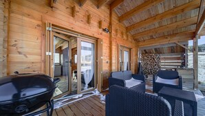 Una cabaña de madera con porche cubierto, mobiliario exterior y una parrilla.