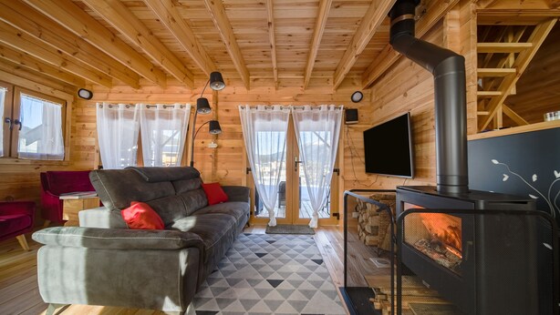 Un interior de cabaña acogedor con sofá, televisión, chimenea y paredes de madera.