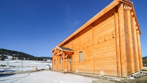 Una cabaña de madera con techo a dos aguas, un porche delantero y un cobertizo pequeño adosado.