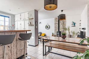 A modern kitchen with a bar area, white cabinets, and a stone accent wall. - La Jeannette - maison avec jardin (Ver-sur-Mer)