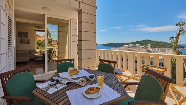 A balcony with a table set for breakfast, including croissants and juice, overlooking a scenic view of a coastal area.