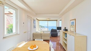 A modern living room with a sofa, a dining table with oranges, and a view of the sea.