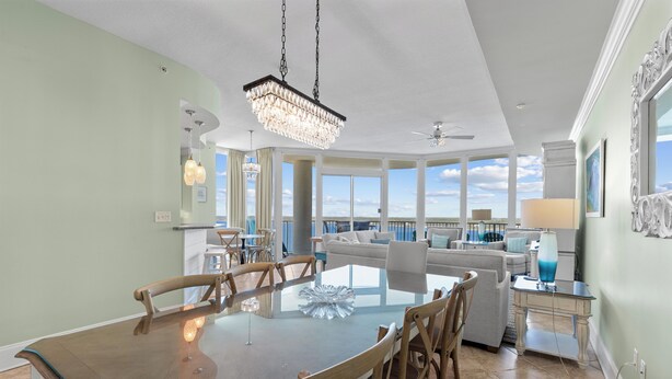 A spacious dining area with a large glass table and wooden chairs, a chandelier, and a view of the ocean through large windows. - Lagoon Front corner unit with lagoon and gulf views! 11th floor 3 bed 3 bath (Gulf Shores)