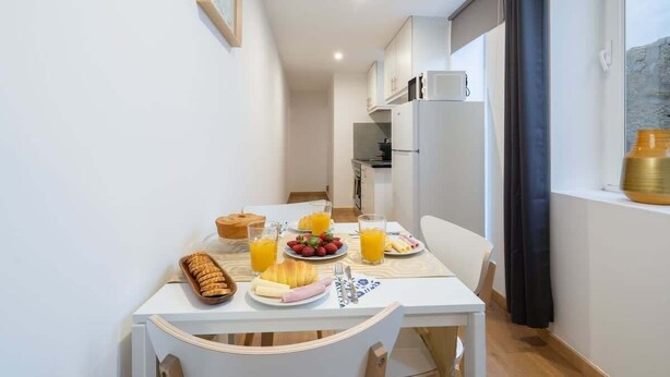 A small, bright kitchen with white cabinets, a white table, and a breakfast setting including croissants, strawberries, and orange juice. - Peaceful & Bright Flat with Terrace by Host Wise (Porto)