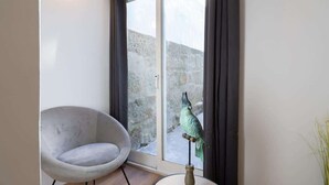 A room with a grey armchair, a small table with a bird sculpture, and a view through a glass door to an outdoor area with stone walls. - Peaceful & Bright Flat with Terrace by Host Wise (Porto)