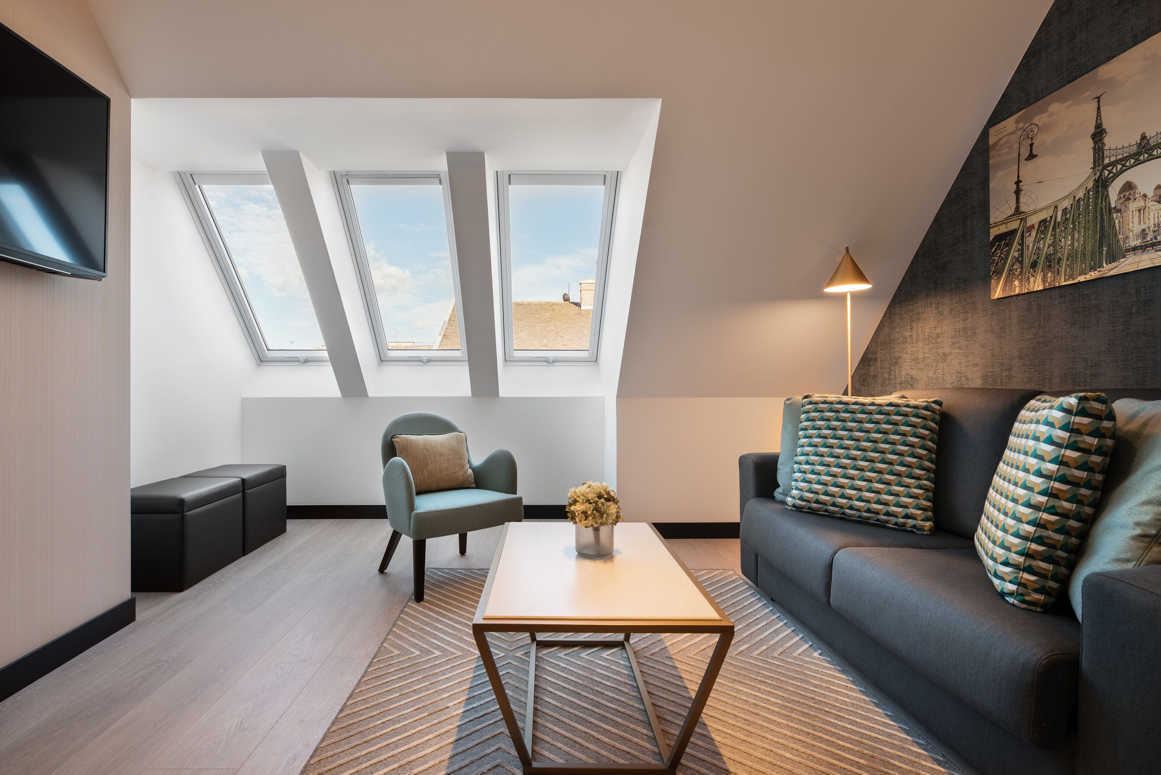 A modern living room with a sofa, a coffee table, and a TV mounted on the wall. There are three skylights allowing natural light into the room.