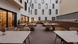 An outdoor dining area with multiple tables and chairs, a wooden deck, and a building with a modern facade in the background. - Eurostars Ambassador (Budapest)