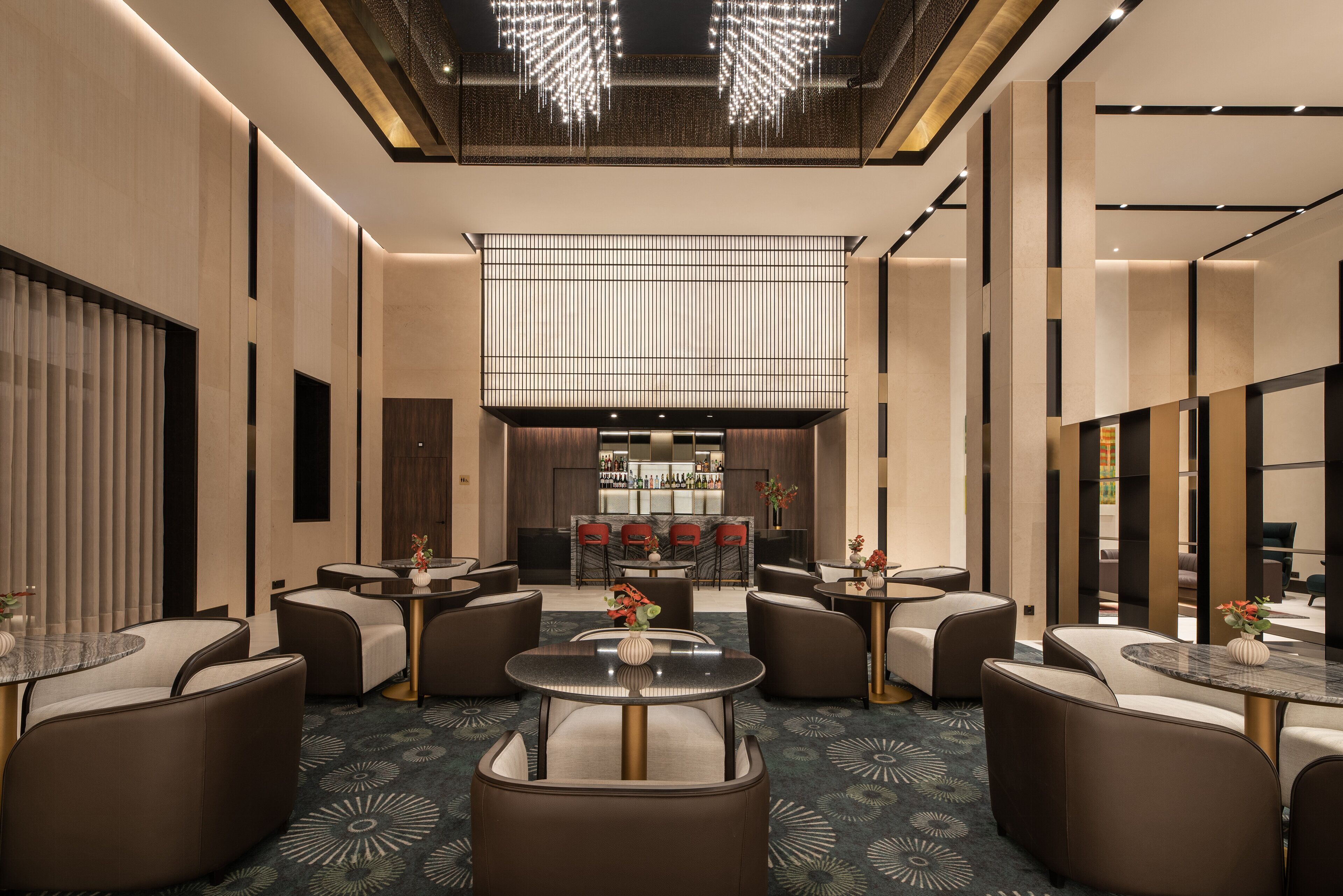 Un'elegante hall d'albergo con tavoli rotondi e divani, una zona bar e un soffitto alto decorato con lampadari.
