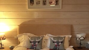 A neatly made bed with a red bedspread, two pillows with reindeer designs, and two folded towels. - A bit of Alpine heaven with stunning views! (Les Allues)