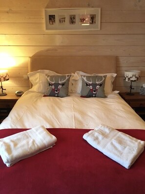 A neatly made bed with a red bedspread, two pillows with reindeer designs, and two folded towels.