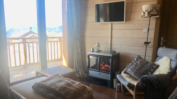 A cozy living room with a fireplace, a television, and a view of a wooden deck. - A bit of Alpine heaven with stunning views! (Les Allues)