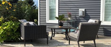 A deck with wicker furniture and a potted plant, adjacent to a house with gray siding and white trim.
