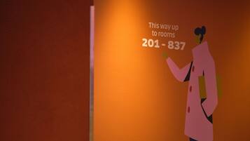 A person in a pink coat pointing to a sign with room numbers 201-837.