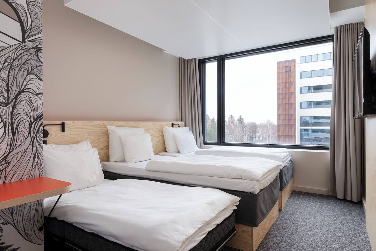 A hotel room with two beds, a TV, and a large window with a view of a building.
