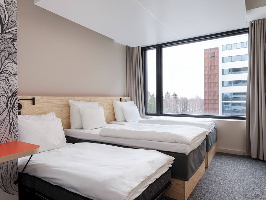 A hotel room with two beds, a TV, and a large window with a view of a building.