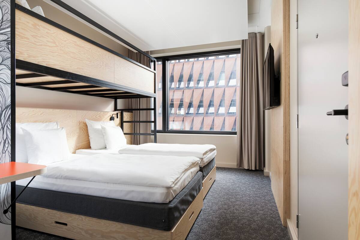 A hotel room with bunk beds, a television, and a window with a city view.