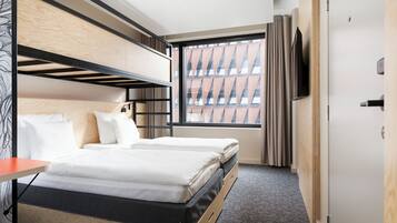 Une chambre d’hôtel avec des lits superposés, une télévision et une fenêtre donnant sur la ville.
