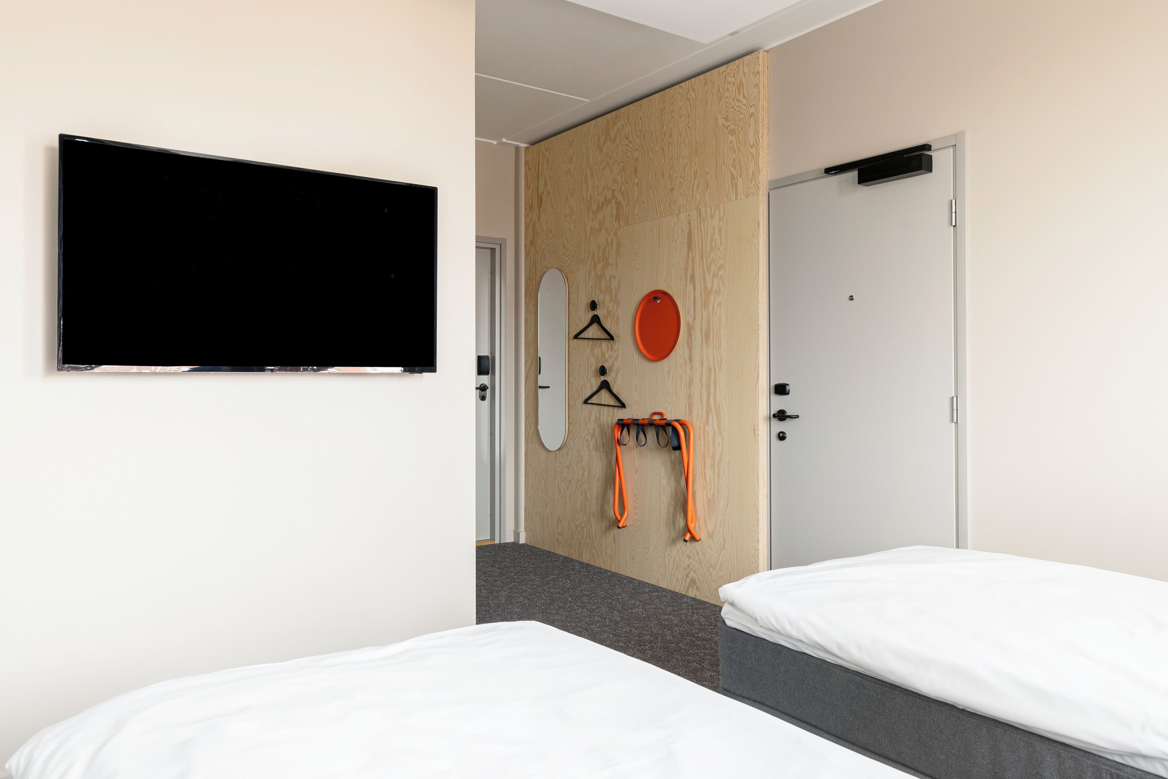 A hotel room with two beds, a TV mounted on the wall, a wooden partition, and a door with a handle.