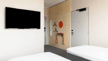 Habitación de hotel con dos camas, un televisor montado en la pared, una separación de madera y una puerta con manija.