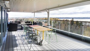 An outdoor deck with a table and chairs, a sofa, and a view of a body of water and trees.