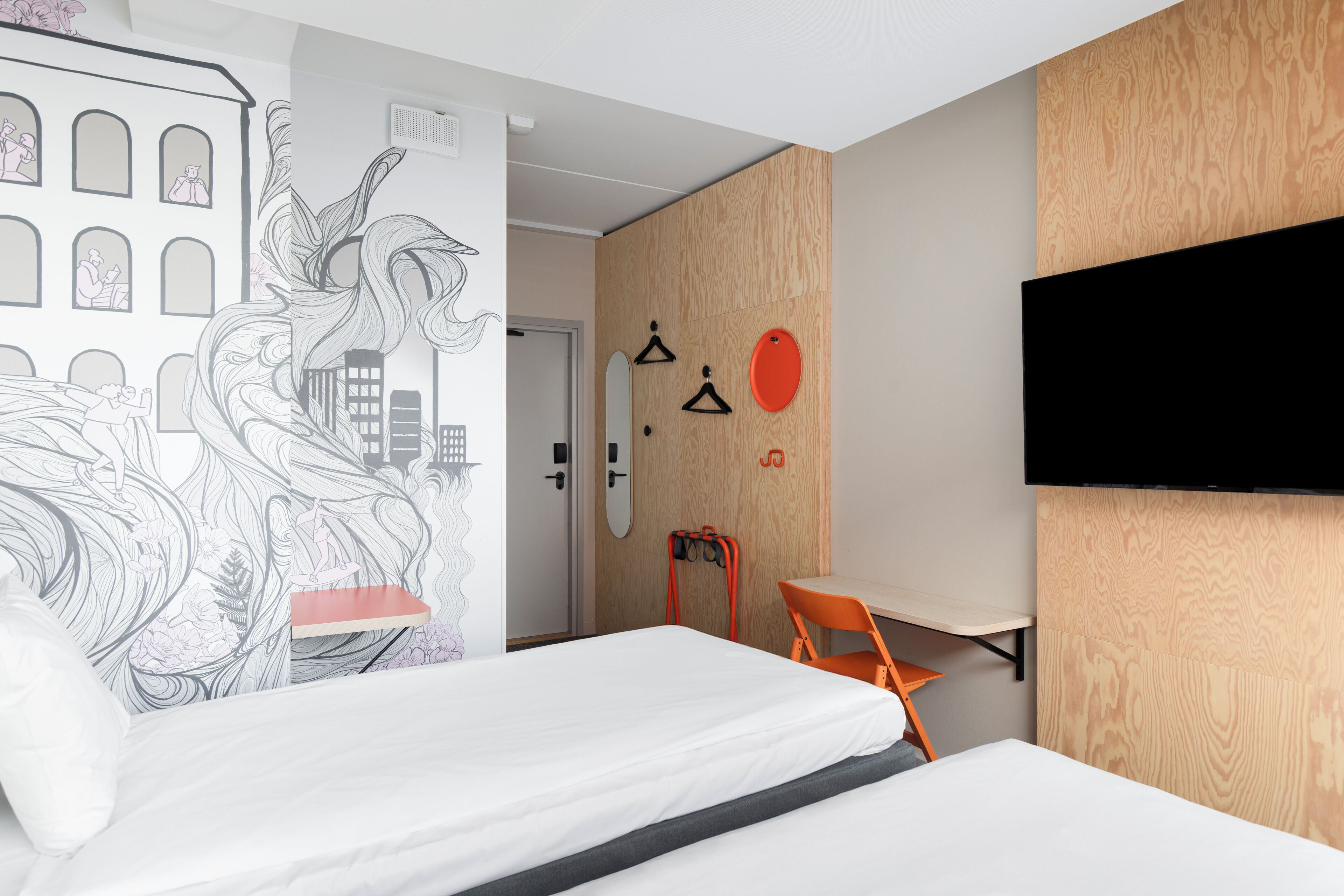 Una habitación de hotel moderna con una cama grande, un escritorio y un televisor instalado en la pared.