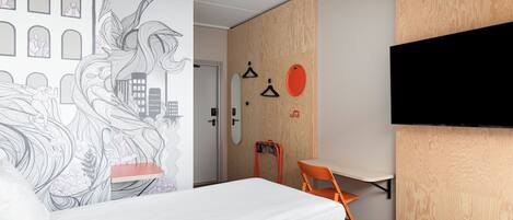 Una habitación de hotel moderna con una cama grande, un escritorio y un televisor instalado en la pared.