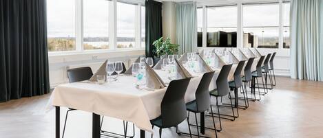 A conference room with a long table set for a meeting, large windows with curtains, and a view of the cityscape.