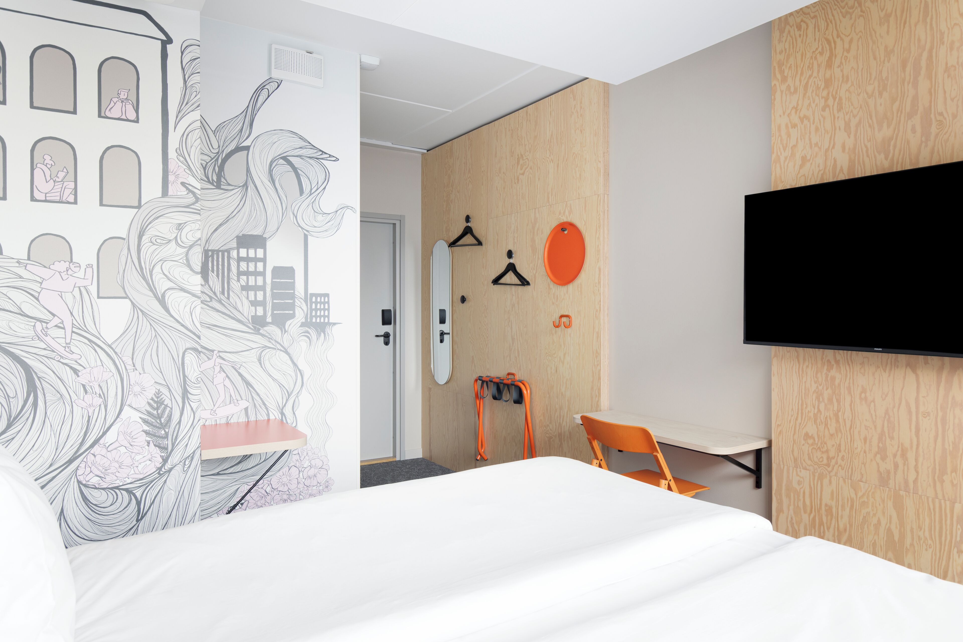 A modern hotel room with a large bed, a flat-screen TV, a wooden accent wall, and a cityscape mural.