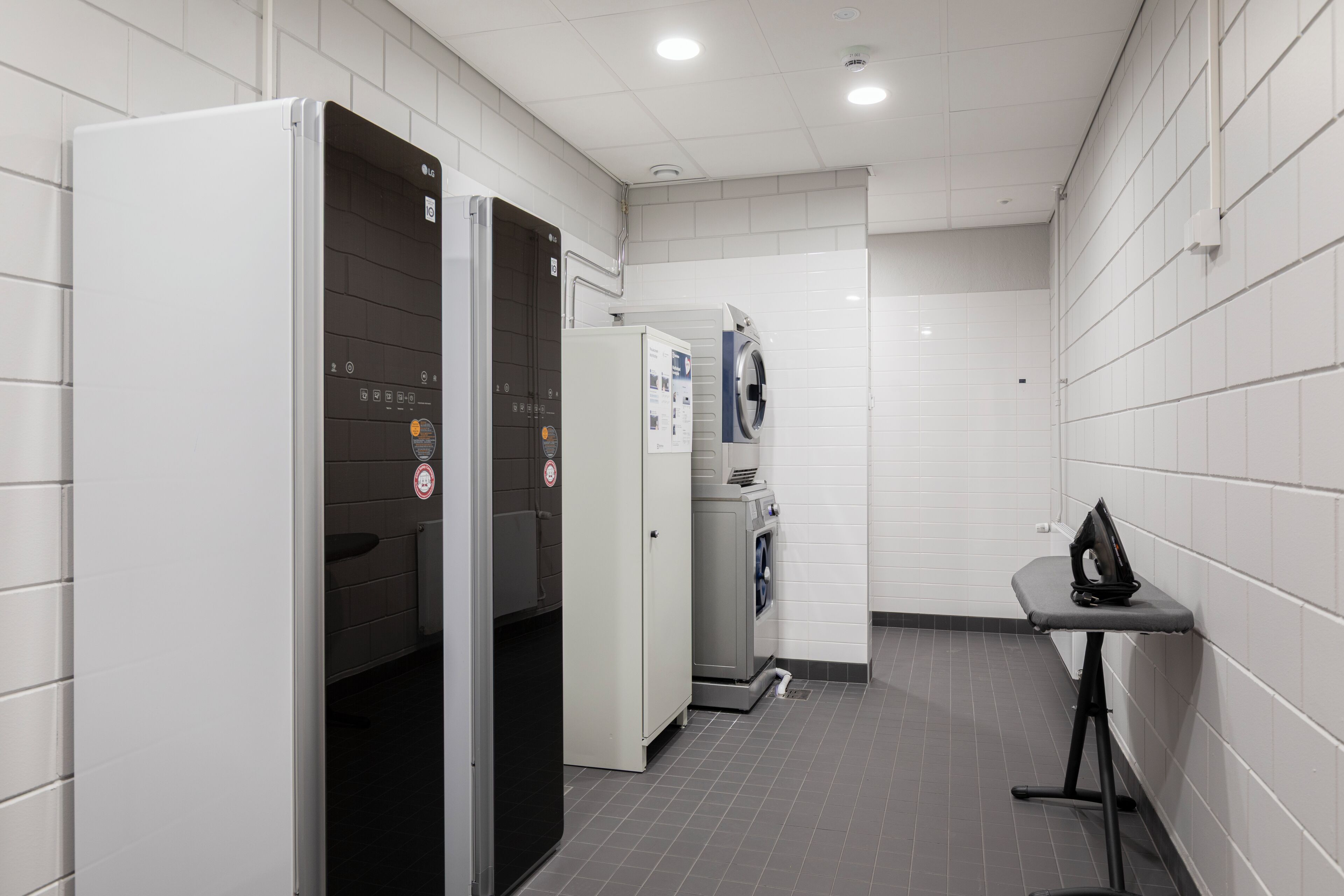A clean, modern bathroom with a white tiled wall, a grey floor, and a small table with a bag on it.