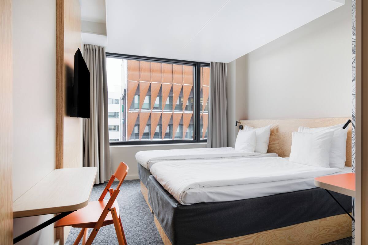 A hotel room with a large window, a bed, a desk, and a chair.