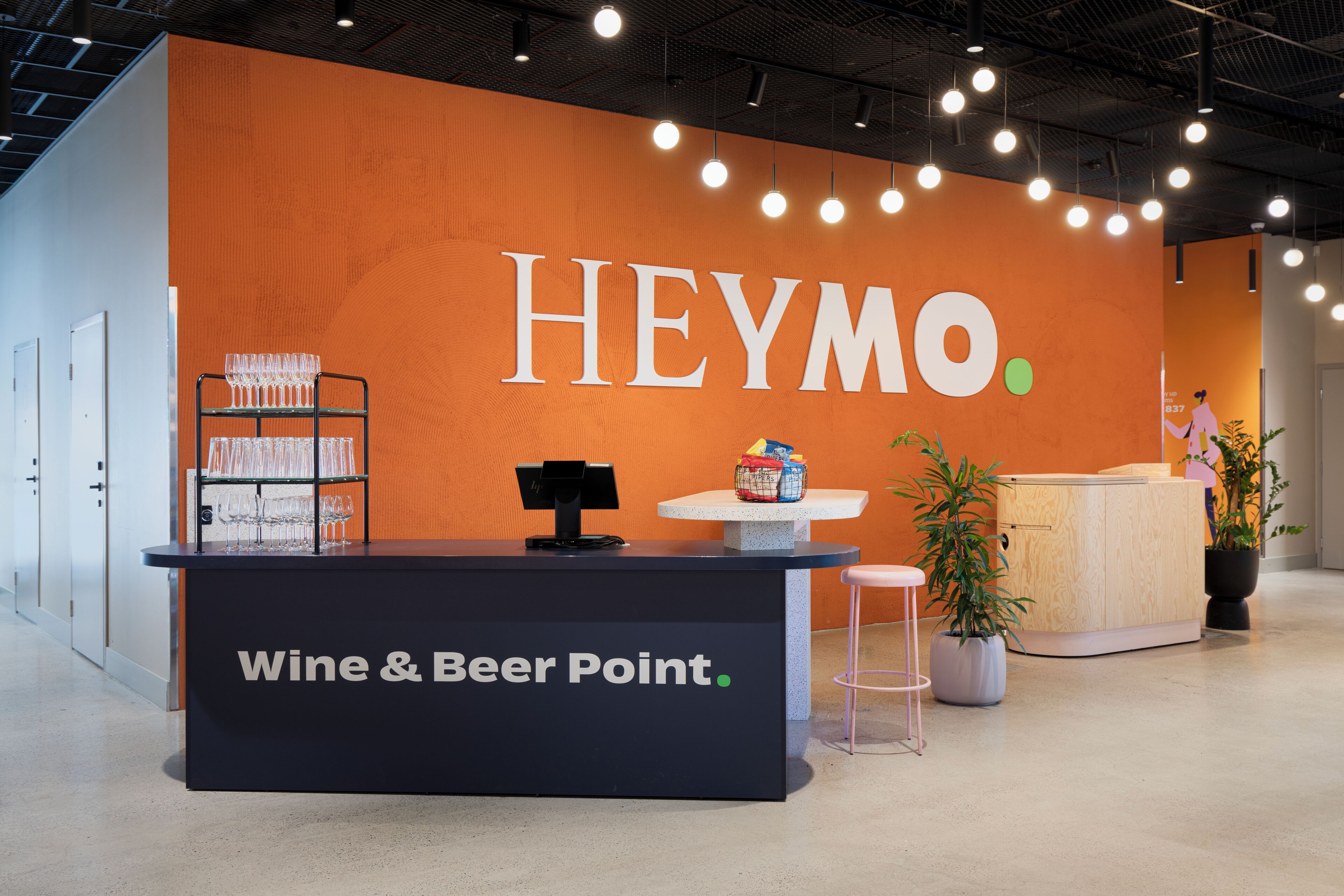 A reception area with a large orange wall, a counter labeled "Wine & Beer Point," and a small table with a plant.