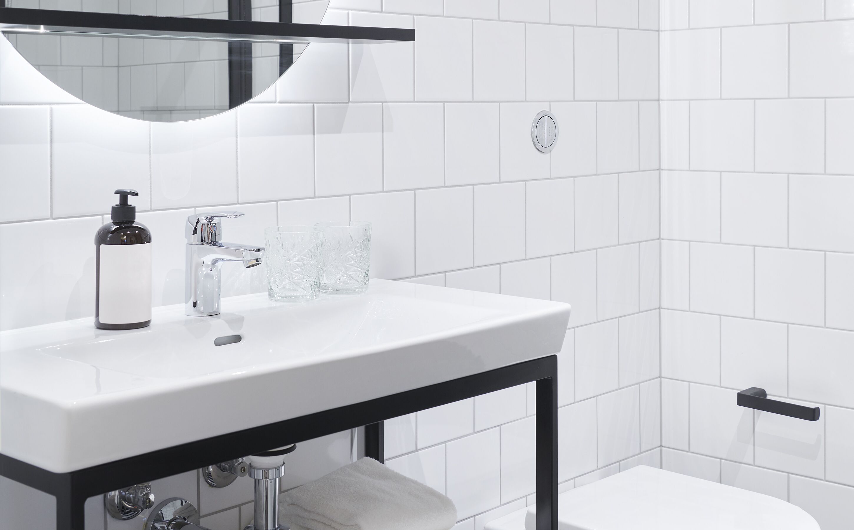 A modern bathroom with a white sink, black faucet, and a glass bottle.