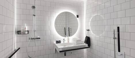 A modern bathroom with white tiled walls, a round mirror, a sink with a towel, and a shower.