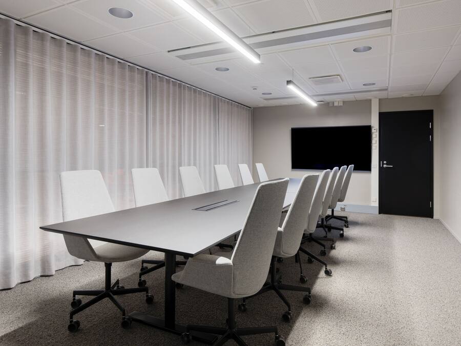 A conference room with a long table, six chairs, a projector screen, and a door.