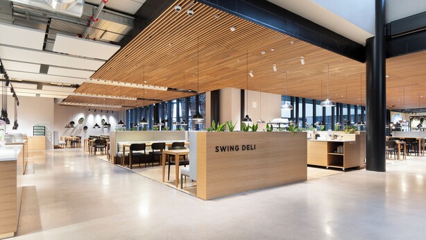A modern office space with a central reception area labeled 'SWING DELI', featuring a wooden slatted ceiling, glass partitions, and a clean, polished floor.