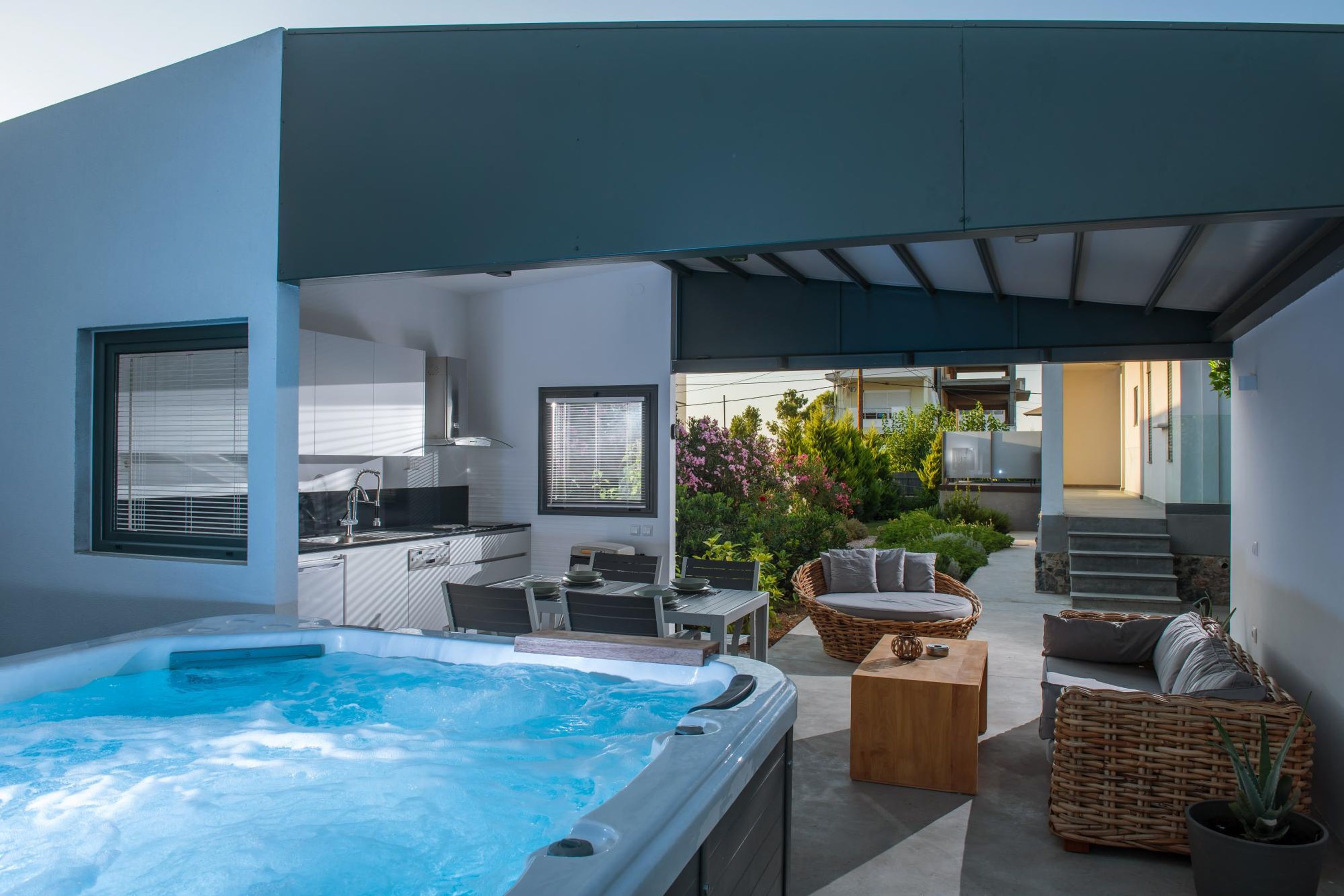 A modern outdoor living area with a hot tub, seating, and a kitchen area.