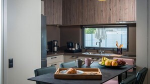 A modern kitchen with wooden cabinets, a black countertop, and a dining table with a tray of food and utensils. - Villa Amo With Private Pool (Malevizi)