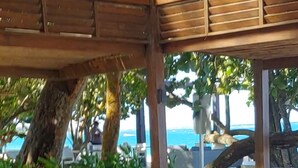 An outdoor seating area with tables and chairs, surrounded by greenery and overlooking a body of water. - Exclusive Beach and Golf Villa with private Hot tub (Puerto Plata)