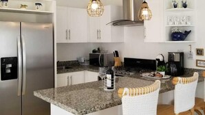 A modern kitchen with a stainless steel refrigerator, granite countertops, and a central island with bar stools. - Exclusive Beach and Golf Villa with private Hot tub (Puerto Plata)