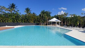A rectangular swimming pool with a white gazebo in the center, surrounded by lounge chairs and palm trees. - Exclusive Beach and Golf Villa with private Hot tub (Puerto Plata)