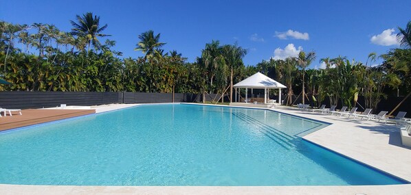 A rectangular swimming pool with a white gazebo in the center, surrounded by lounge chairs and palm trees. - Exclusive Beach and Golf Villa with private Hot tub (Puerto Plata)