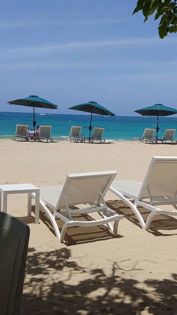 Une plage avec des chaises longues blanches et des parasols verts.